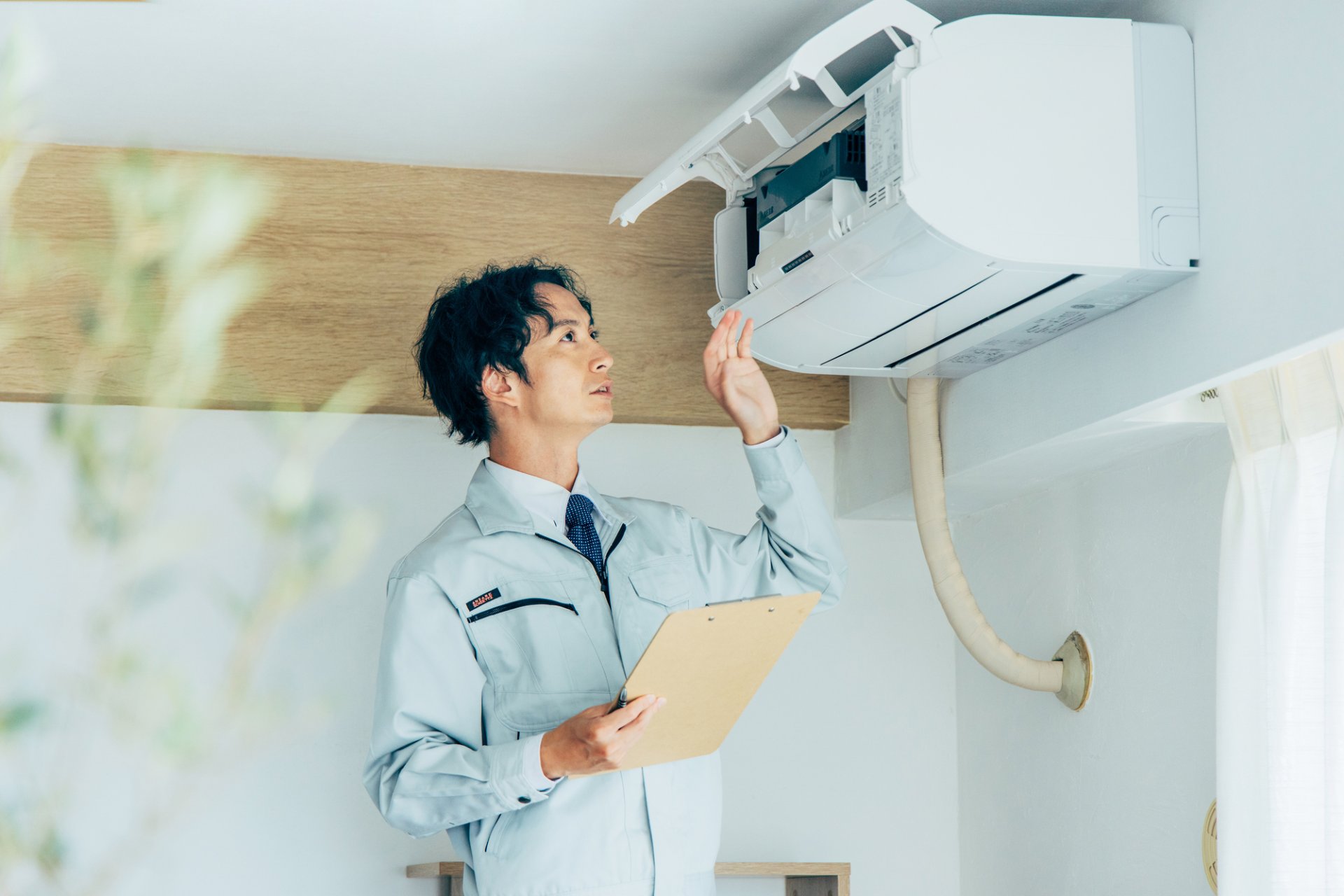一般住宅のリビングに設置された壁掛形エアコンを脚立から点検している作業風景